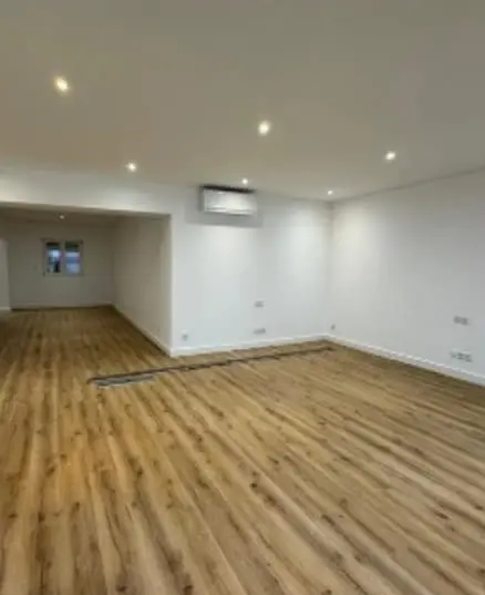 Sala ampla renovada, com pavimento em madeira e iluminação embutida.