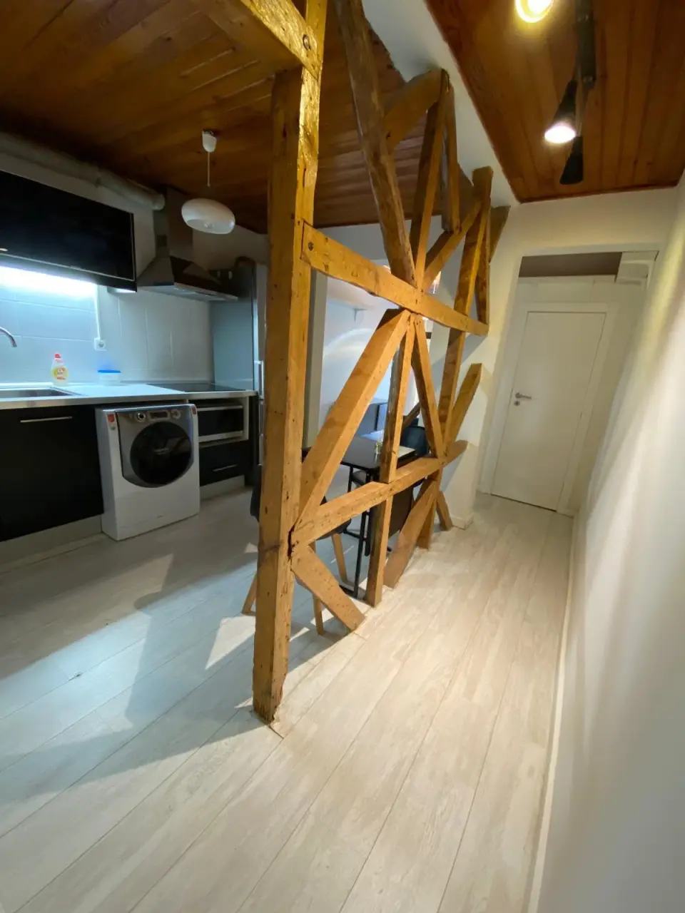 Cozinha com móveis pretos e máquina de lavar roupa, junto às vigas de madeira.