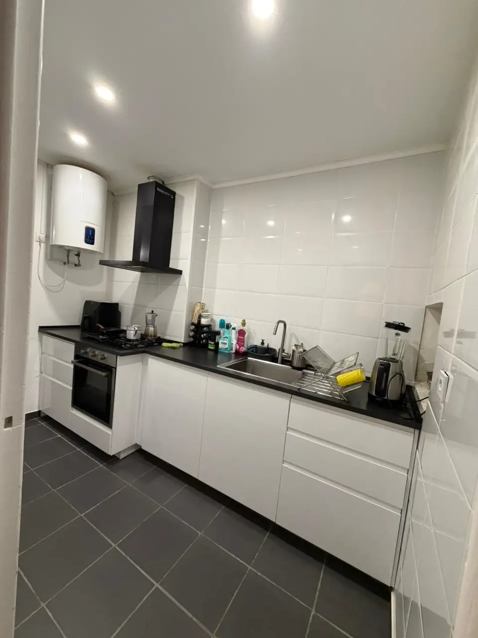 Cozinha com termoacumulador, placa a gás, forno encastrado e bancada preta.