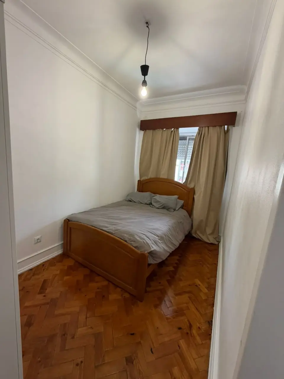 Quarto com soalho em espinha, cama de casal e cortinados.
