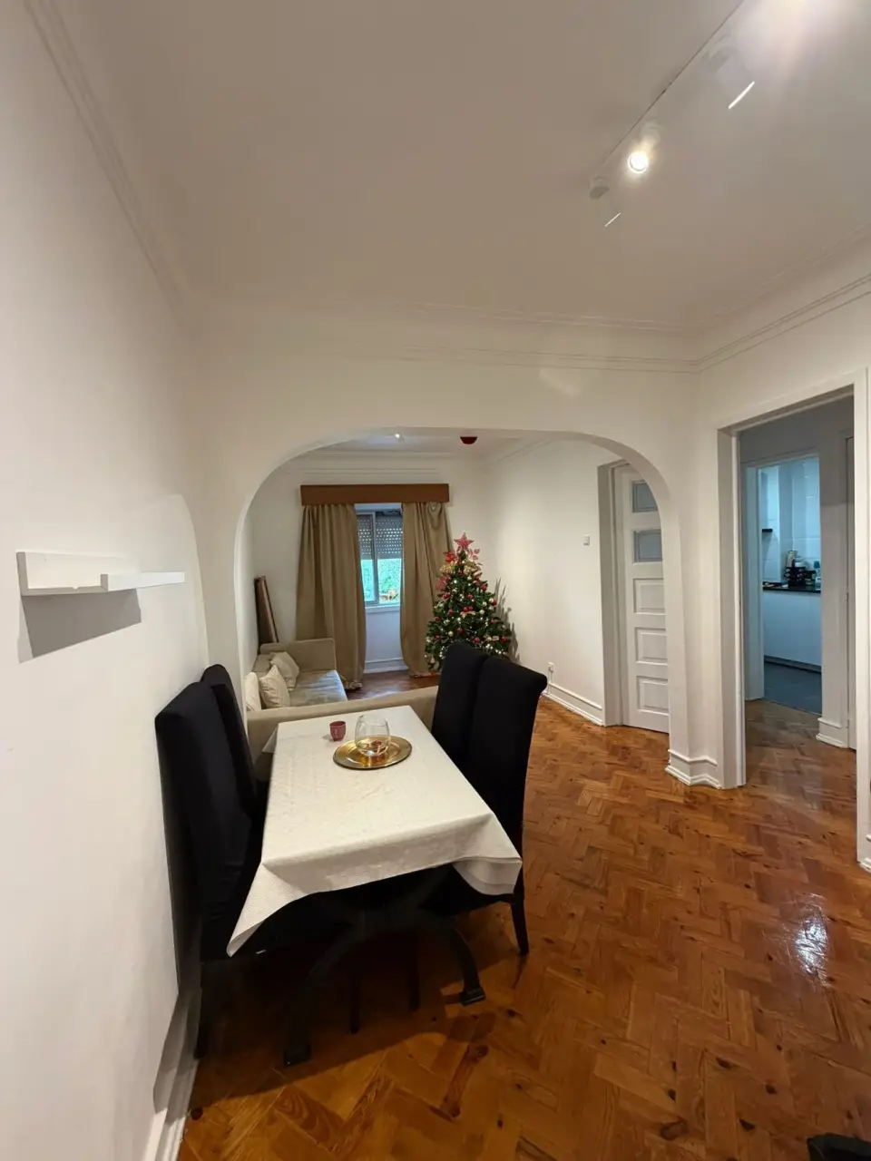 Sala de jantar com arco, soalho em espinha e mesa para quatro pessoas.